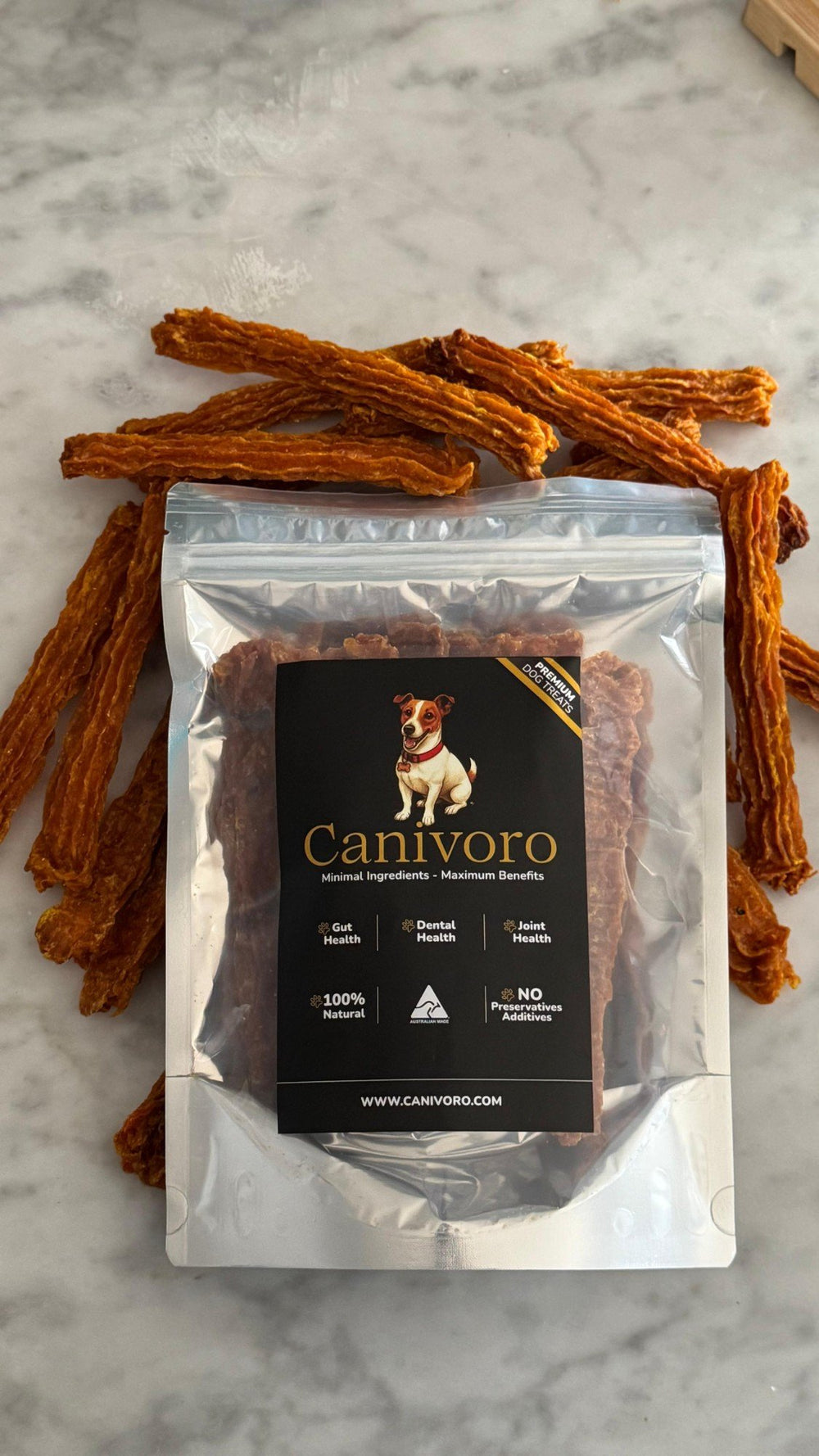 Canivoro Chicken Prime Sticks pouch on white marble, surrounded by golden dried chicken sticks